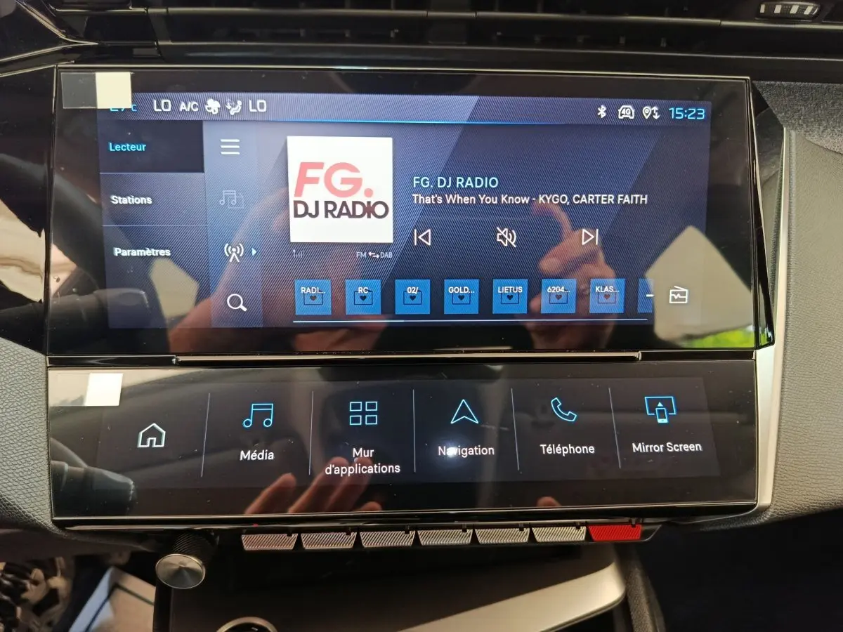 Écran tactile central de la Peugeot 308 gris foncé, affichant la radio FG DJ Radio en intérieur.