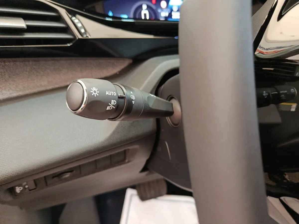 Gros plan sur la commande des phares à gauche du volant cuir dans l’habitacle gris foncé de la Peugeot 308 2026.