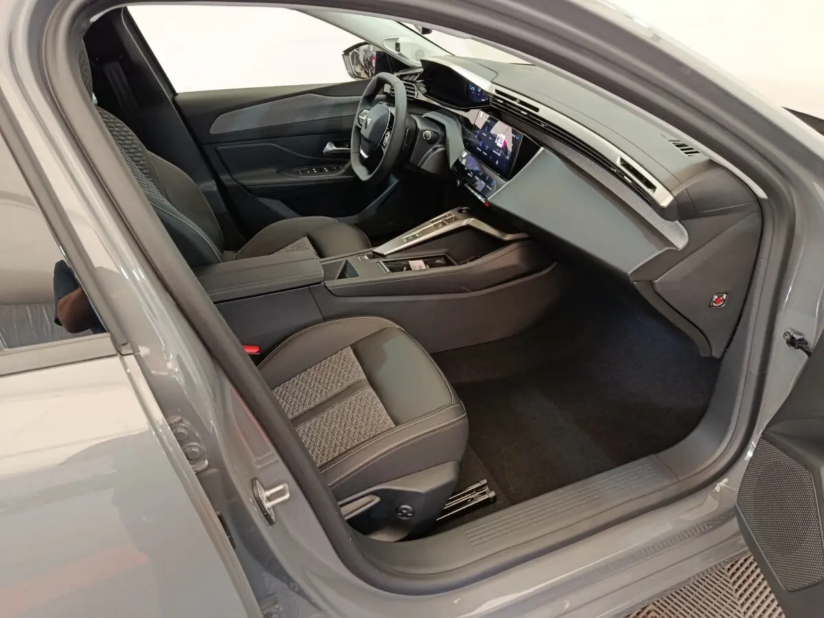 Intérieur avant droit de la Peugeot 308 gris foncé 2026, avec volant cuir multifonctions et écran tactile central.