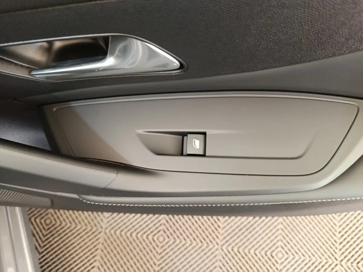 Détail de la commande de lève-vitre côté conducteur sur la porte intérieure d'une Peugeot 308 gris foncé 2026.