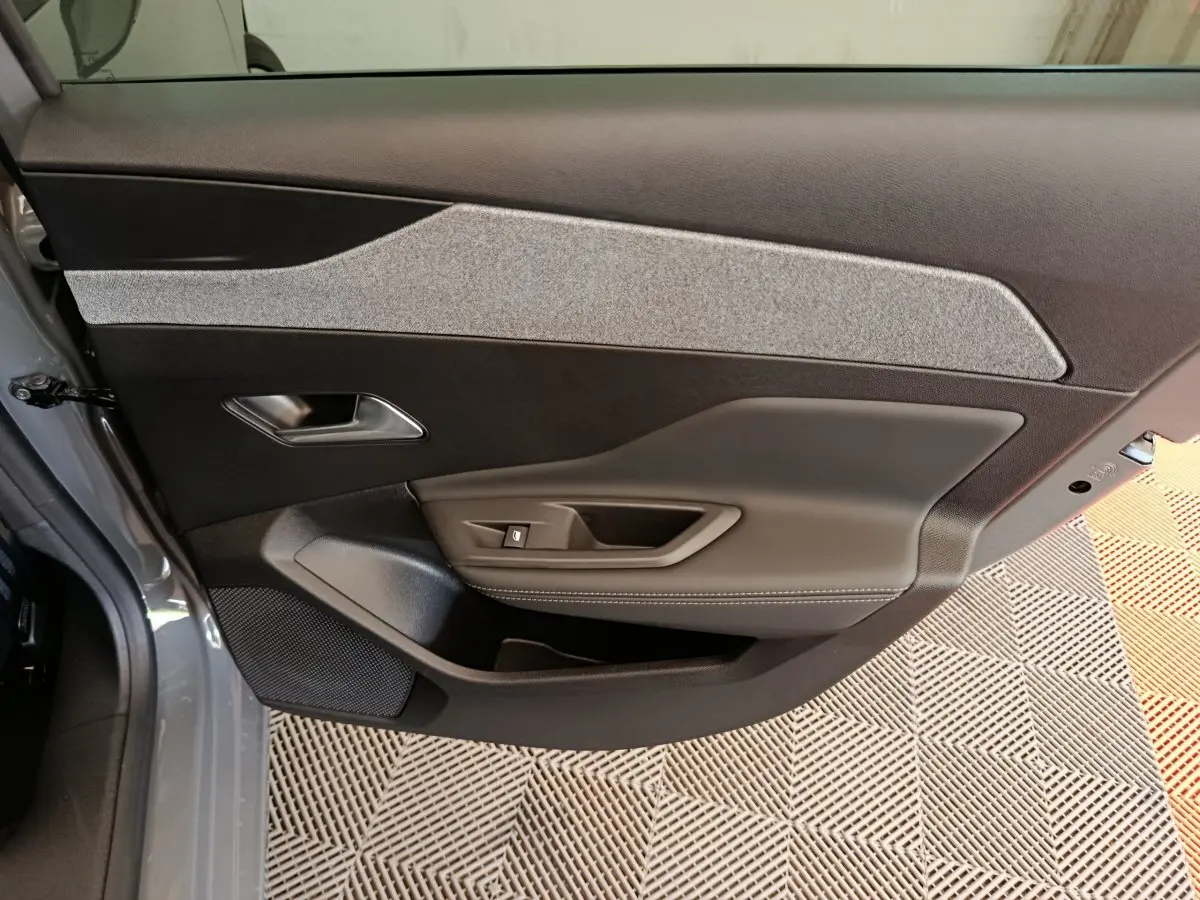 Vue intérieure de la porte avant gauche de la Peugeot 308 gris foncé, avec garniture tissu et commandes de fenêtre.