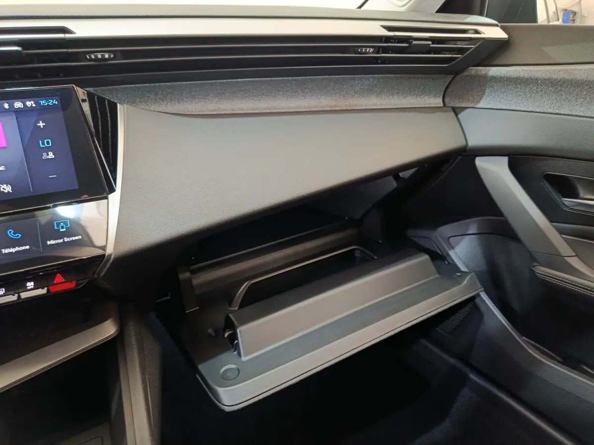 Intérieur de la Peugeot 308 2026 gris foncé, vue côté passager sur la boîte à gants ouverte et tableau de bord moderne.