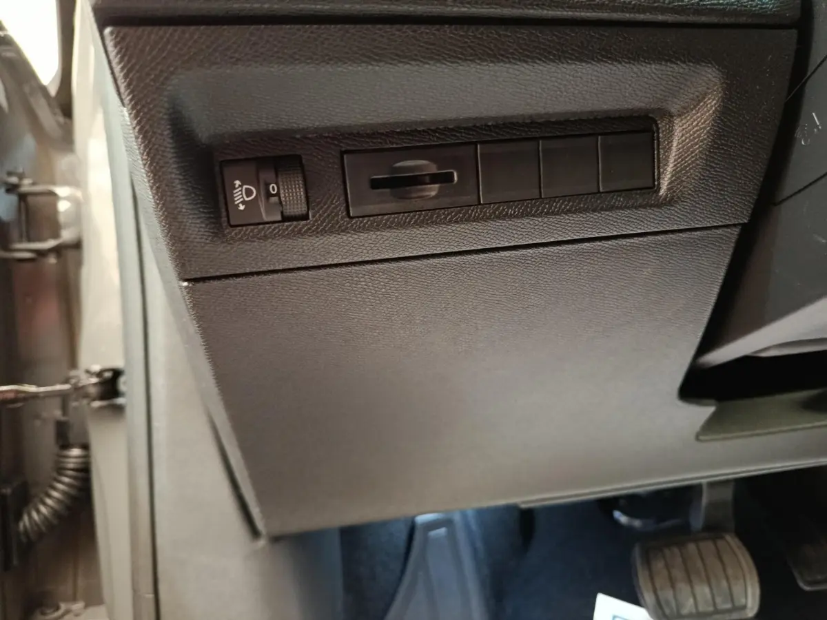 Vue intérieure côté conducteur de la Peugeot 308 gris foncé, avec commandes d'éclairage et pédales visibles.