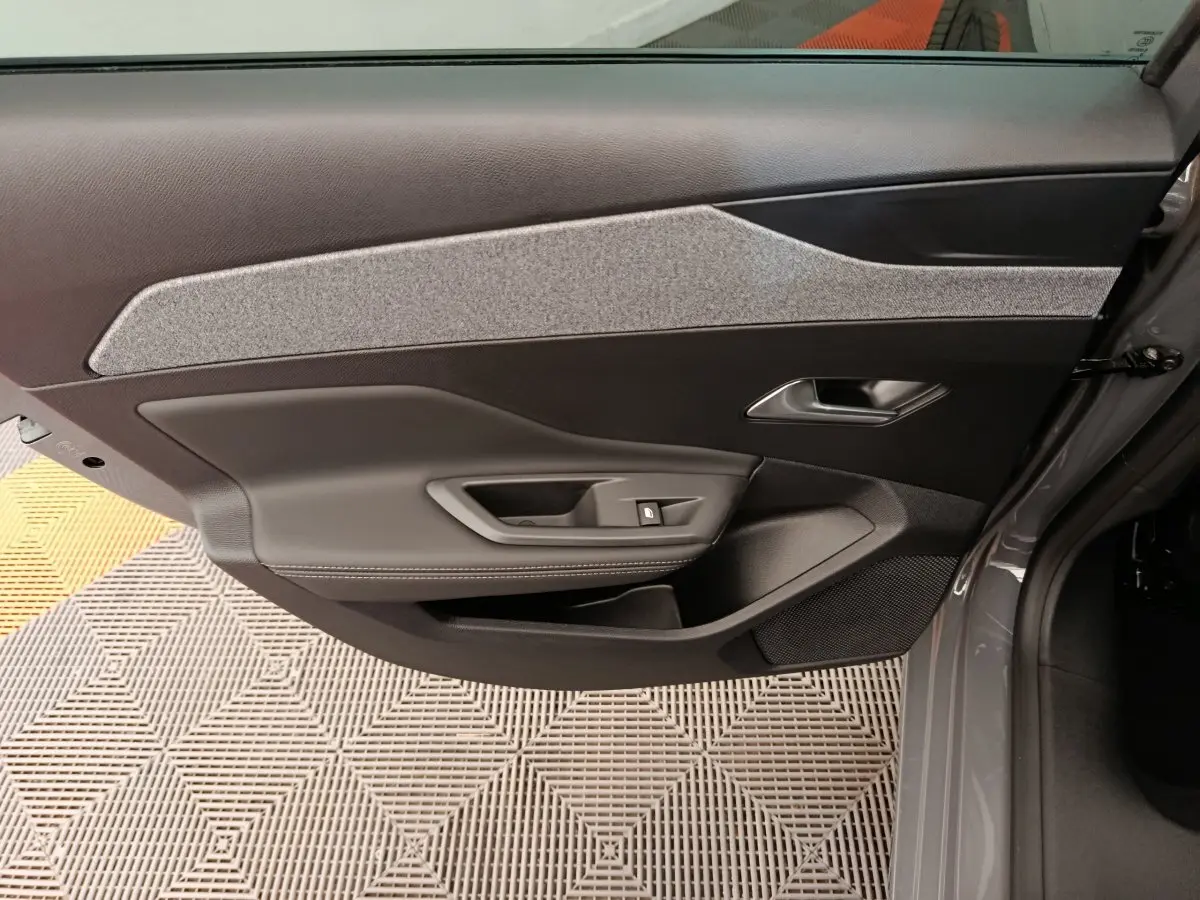 Vue intérieure de la porte avant droite gris foncé de la Peugeot 308 2026 avec insert tissu clair et commande de vitre.