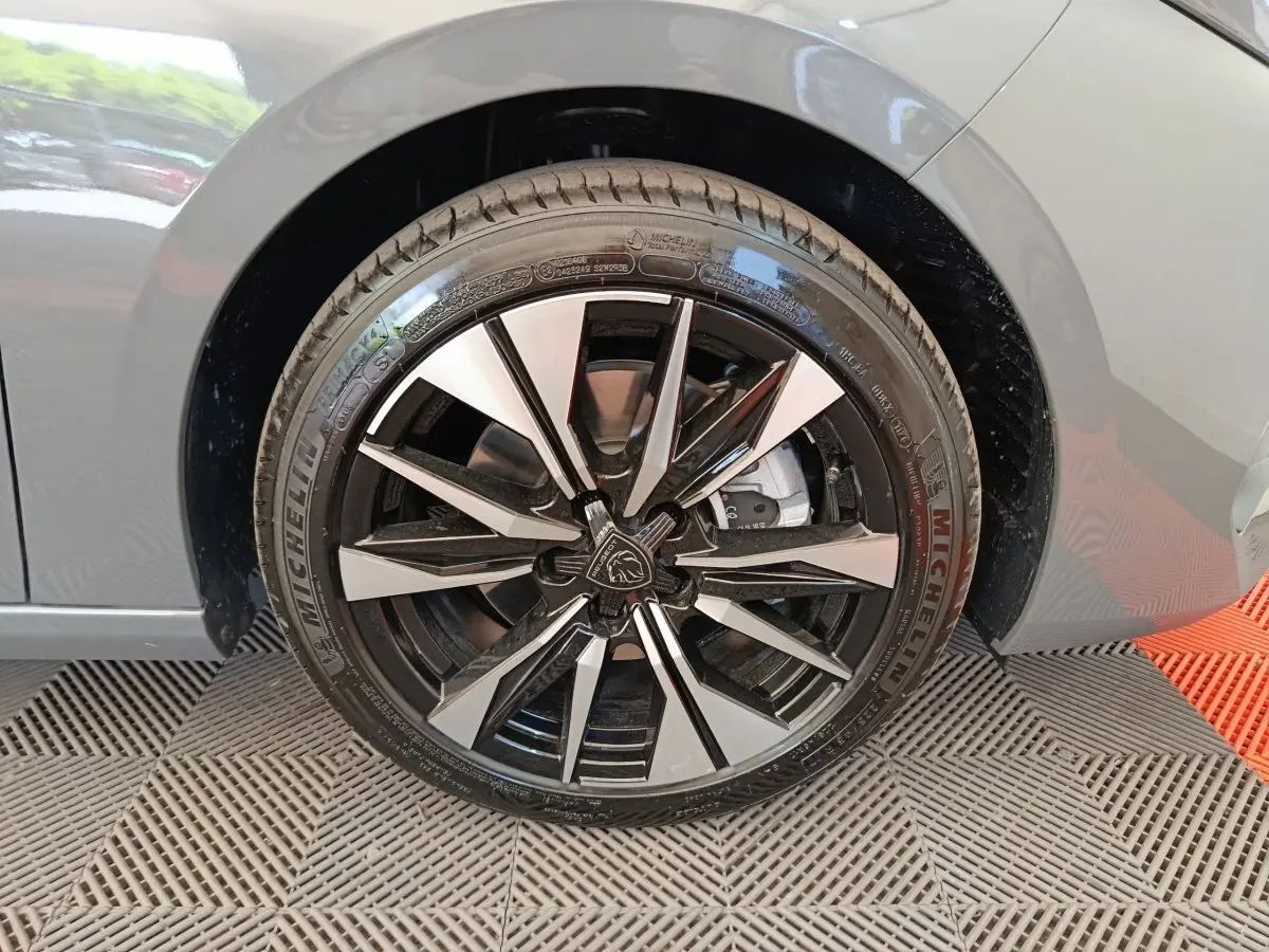Gros plan sur la roue avant droite d’une Peugeot 308 gris foncé, jante alliage noir et argentée au design moderne.