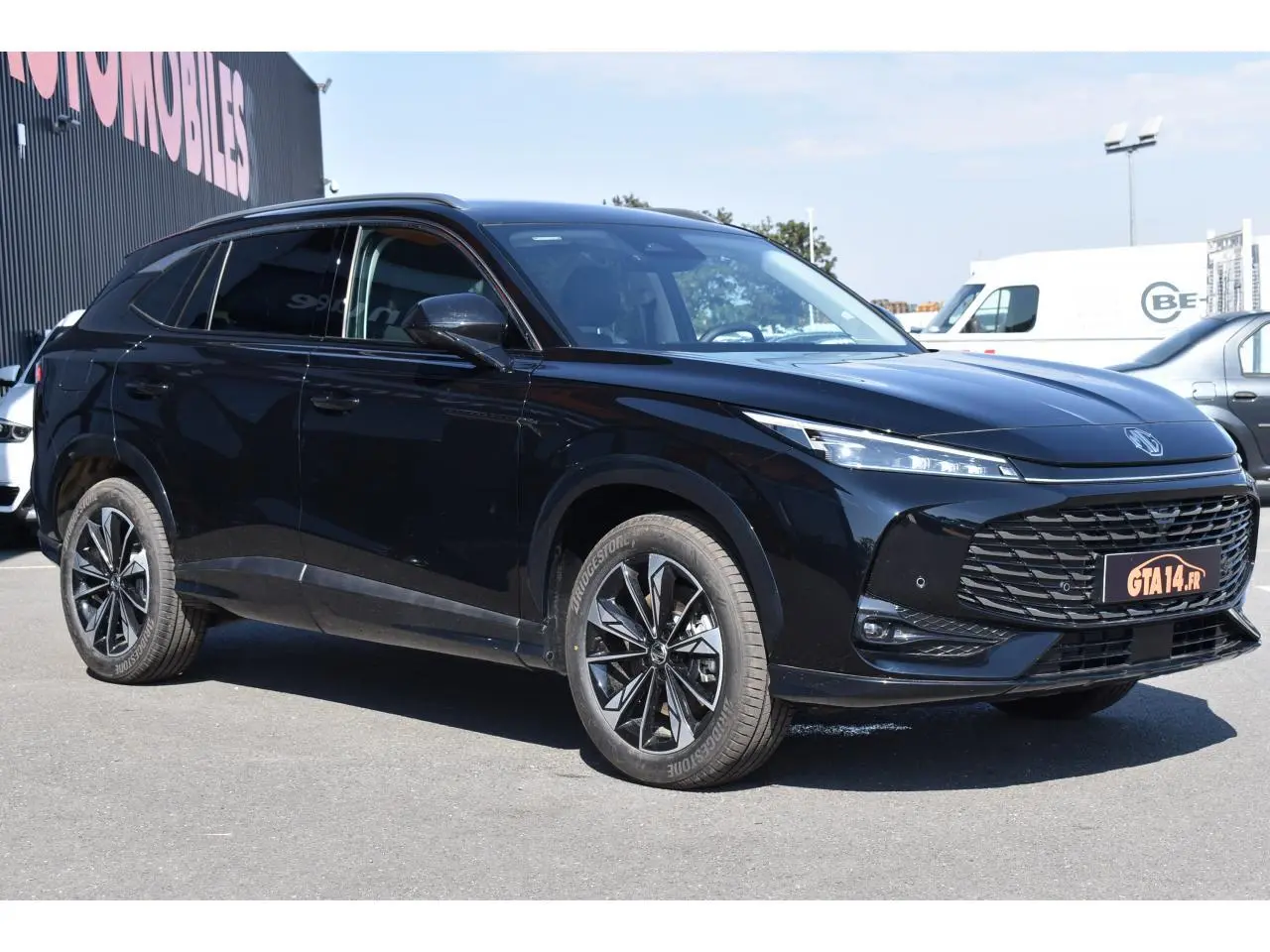 MG Motor EHS 1.5 Hybrid+ noir métallisé en 3/4 avant droit, avec calandre large et jantes alliage 19 pouces.
