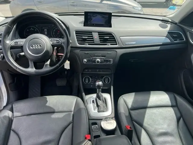 Intérieur de l'Audi Q3 blanc de 2015, vue frontale du tableau de bord avec écran central et volant multifonction.