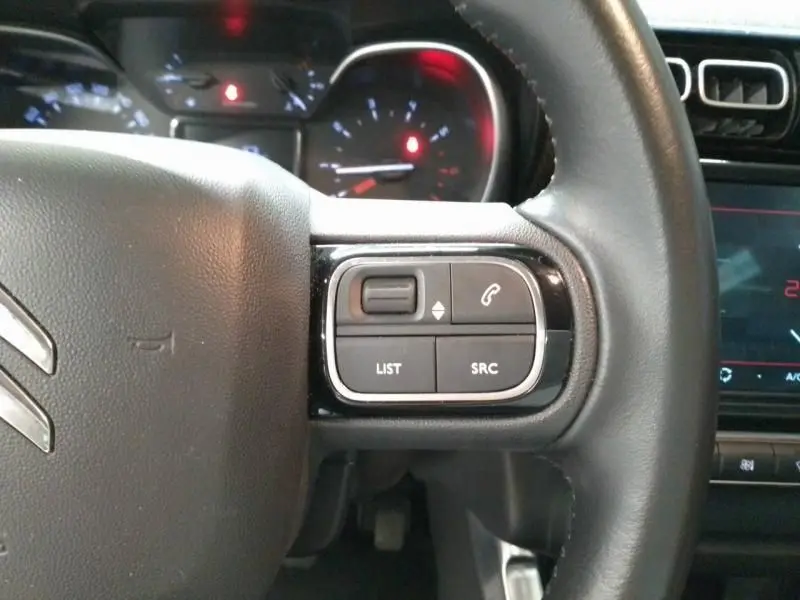 Gros plan sur les commandes à droite du volant en cuir noir du Citroën C3 Aircross gris, tableau de bord en arrière-plan flou.