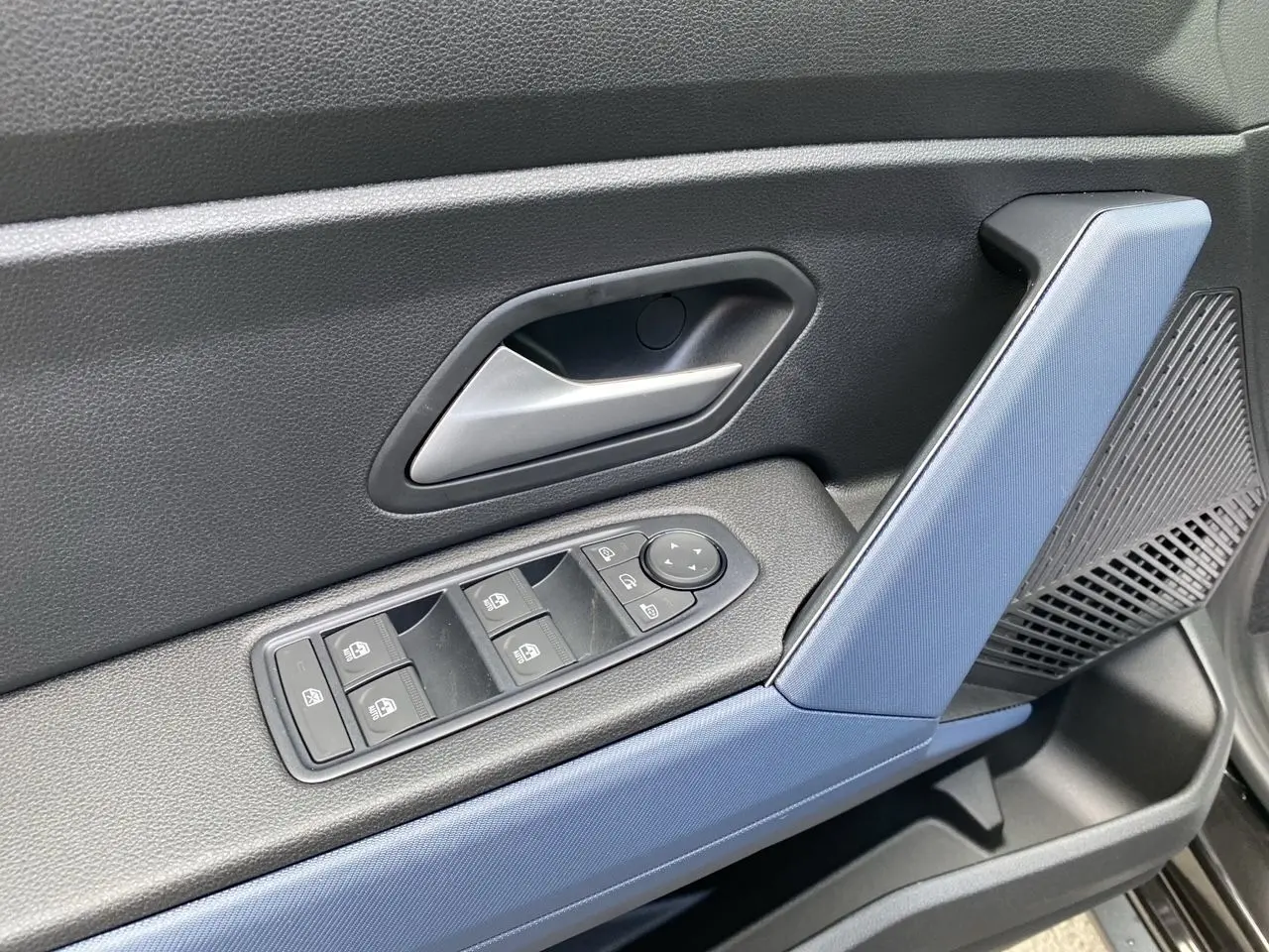 Détail de la porte avant gauche intérieure du Dacia Duster 2025 hybride, avec accoudoir bleu et commandes électriques.