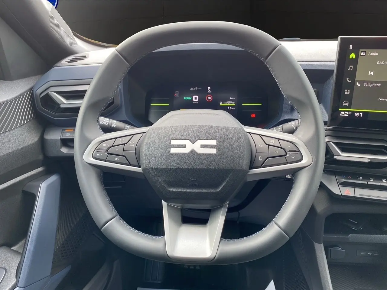 Vue rapprochée du volant noir et gris du Dacia Duster hybride 2025 avec tableau de bord numérique et écran central tactile.