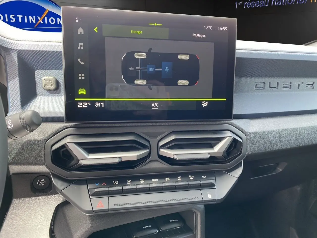 Vue rapprochée du tableau de bord du Dacia Duster hybride 2025, avec écran tactile et aérateurs hexagonaux noirs.