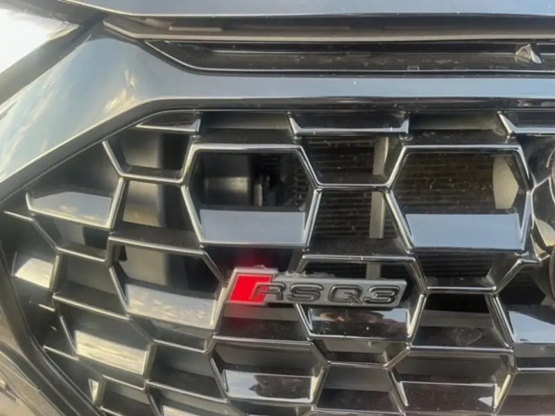 Gros plan sur la calandre noire Mythic de l'Audi RS Q3 Sportback avec logo RS Q3 rouge et argenté.