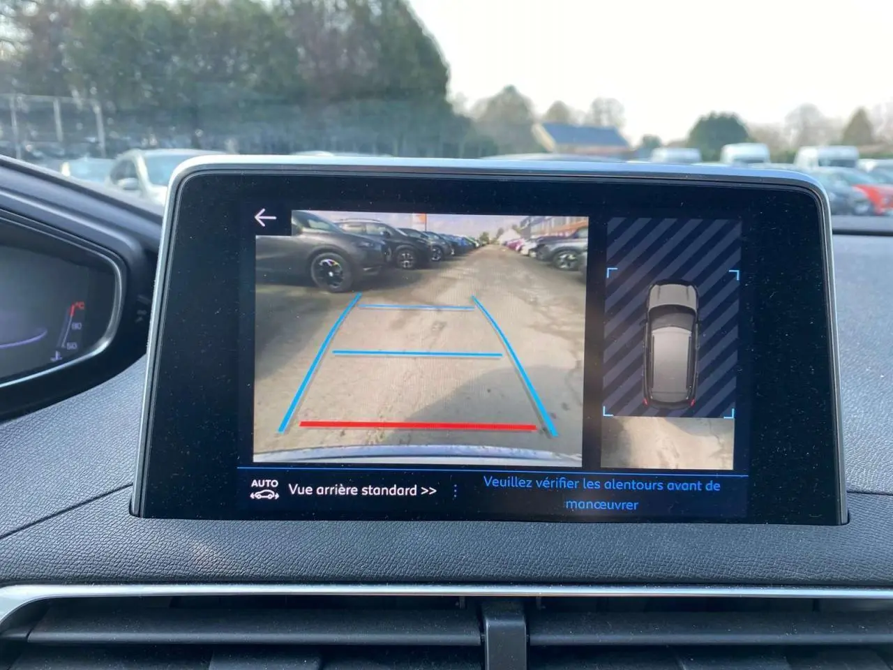 Écran de la Peugeot 3008 blanc montrant l'aide au stationnement arrière avec caméra et guidage graphique bleu et rouge.
