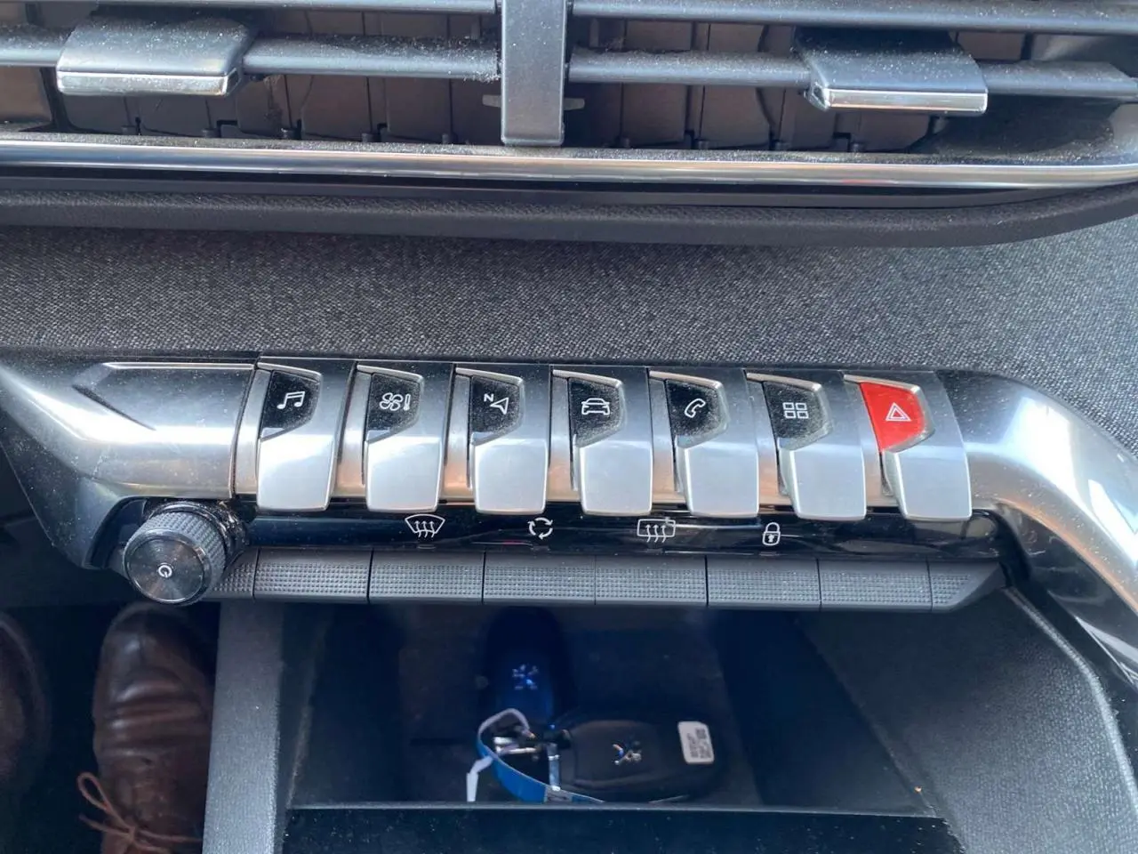 Gros plan sur la rangée de boutons chromés de la console centrale du Peugeot 3008 blanc, avec la clé posée dessous.