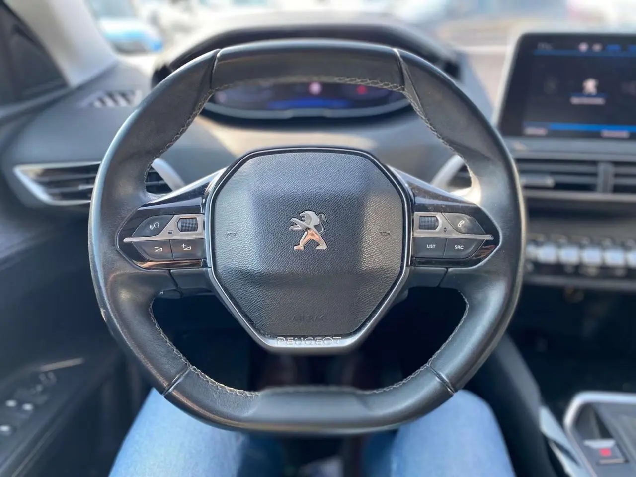 Volant en cuir noir de Peugeot 3008 2018 vu de face, avec commandes intégrées et tableau de bord flou en arrière-plan.