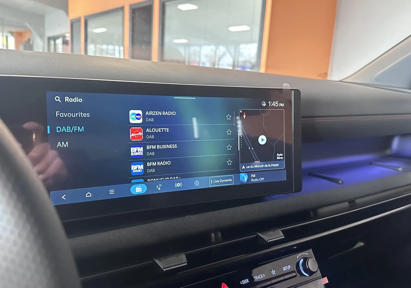 Vue intérieure du tableau de bord du Hyundai Tucson 2025 avec écran tactile affichant les options radio et ambiance lumineuse bleue.