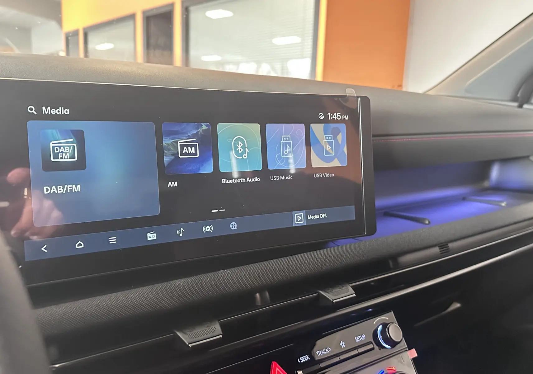 Vue intérieure du tableau de bord du Hyundai Tucson 2025, écran tactile large avec ambiance lumineuse bleue et surpiqûres rouges.