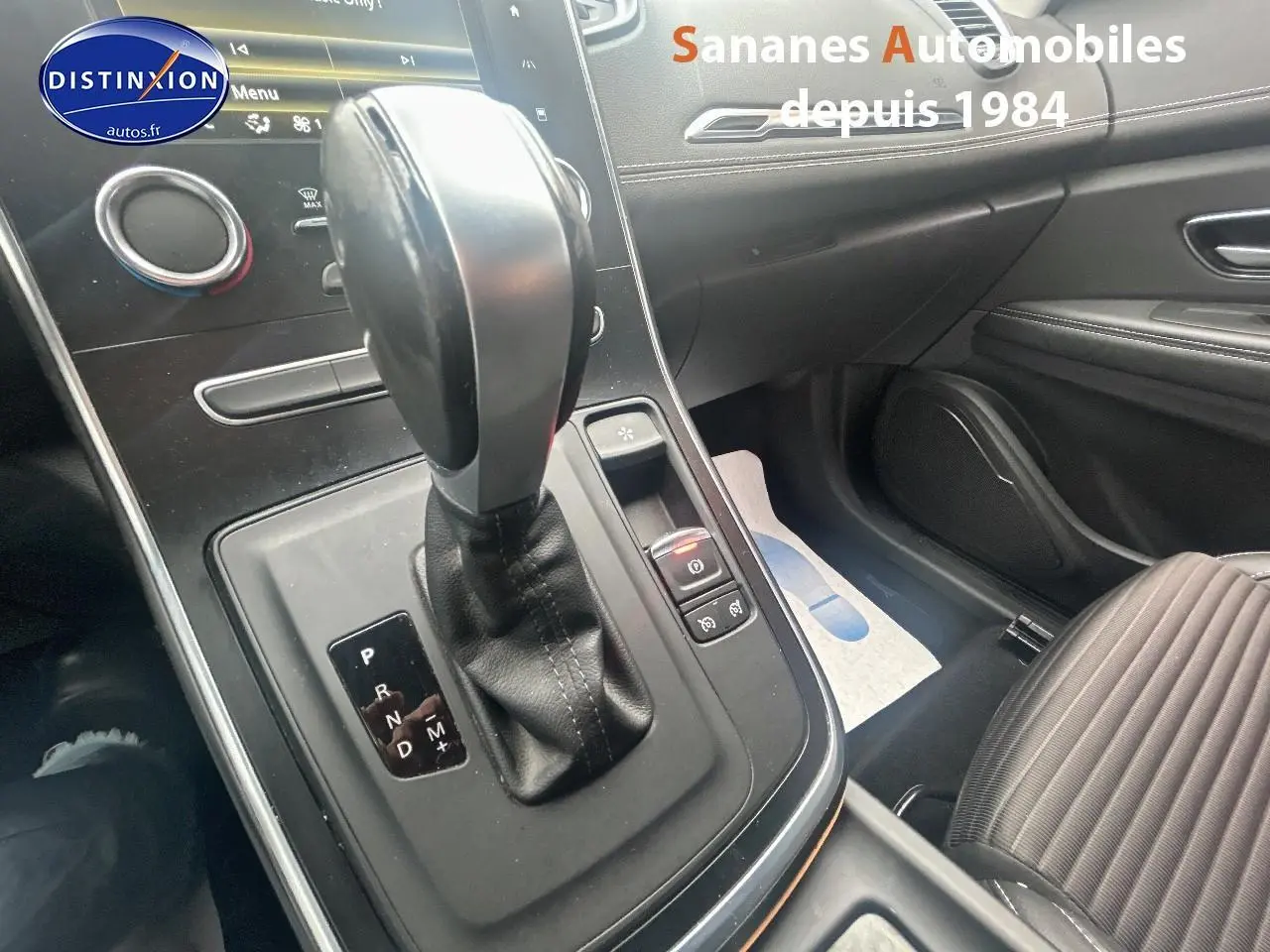 Gros plan sur la console centrale et levier de vitesse automatique du Renault Scénic blanc, intérieur noir avec sellerie tissu.