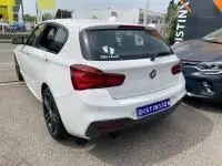 BMW Série 1 114d M Sport blanche vue en 3/4 arrière droit, avec jantes noires et feux arrière rouges.