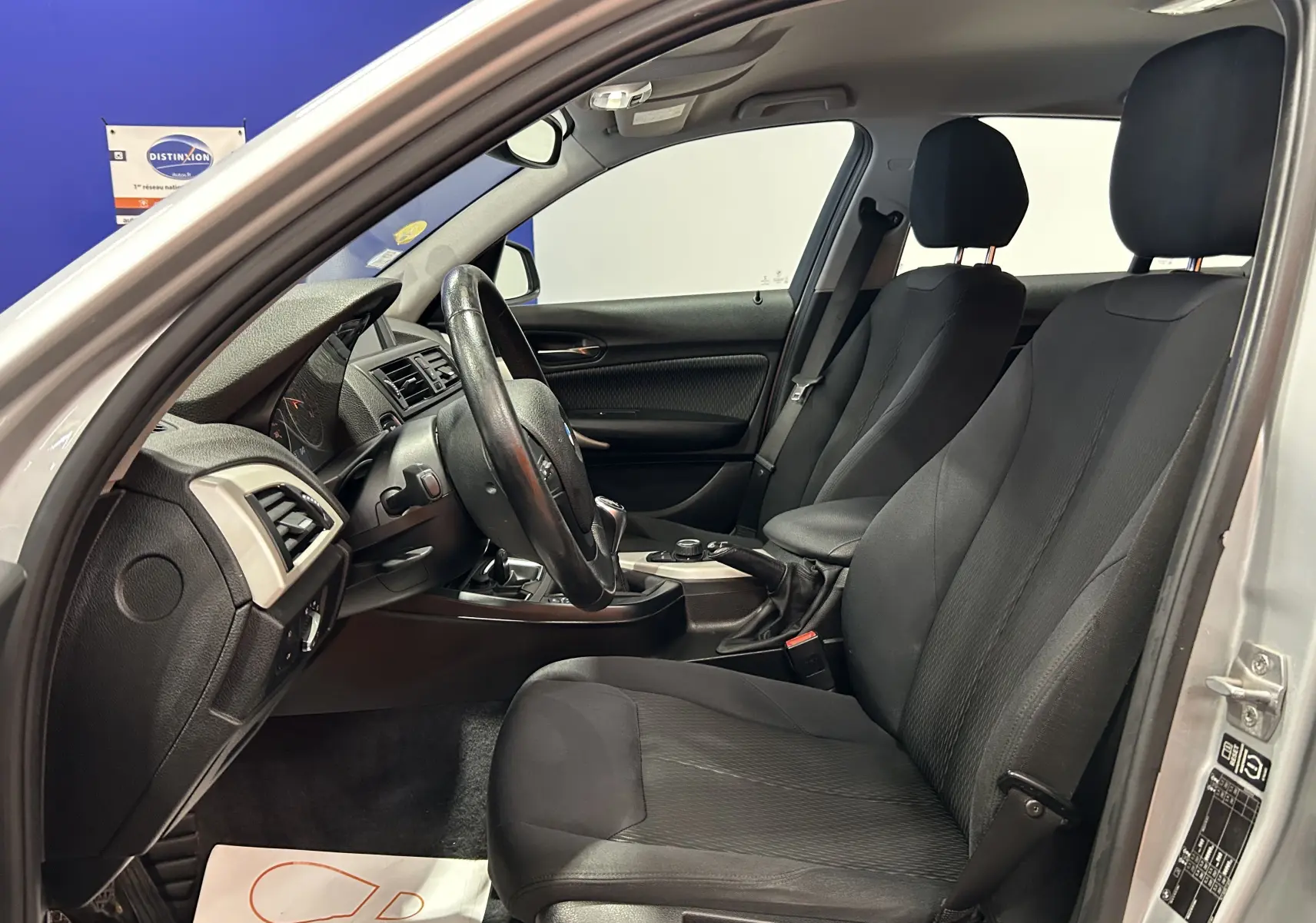 Intérieur avant côté conducteur d'une BMW Série 1 gris 2014, sièges tissu noirs et volant multifonctions.