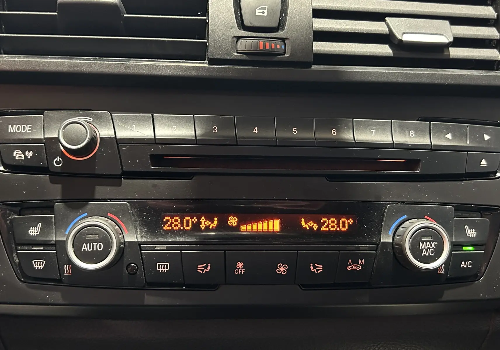 Tableau de bord de BMW Série 1 gris 2014, vue rapprochée sur la console de climatisation digitale affichant 28°C.