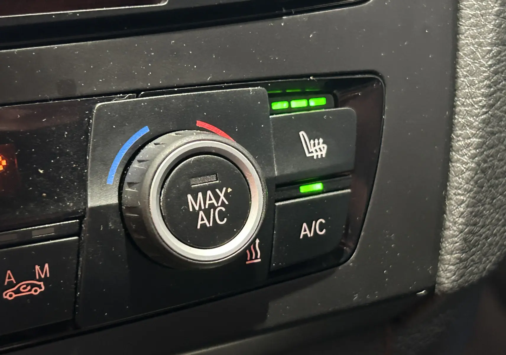 Gros plan sur les commandes de climatisation et siège chauffant activé dans une BMW Série 1 gris diesel de 2014.