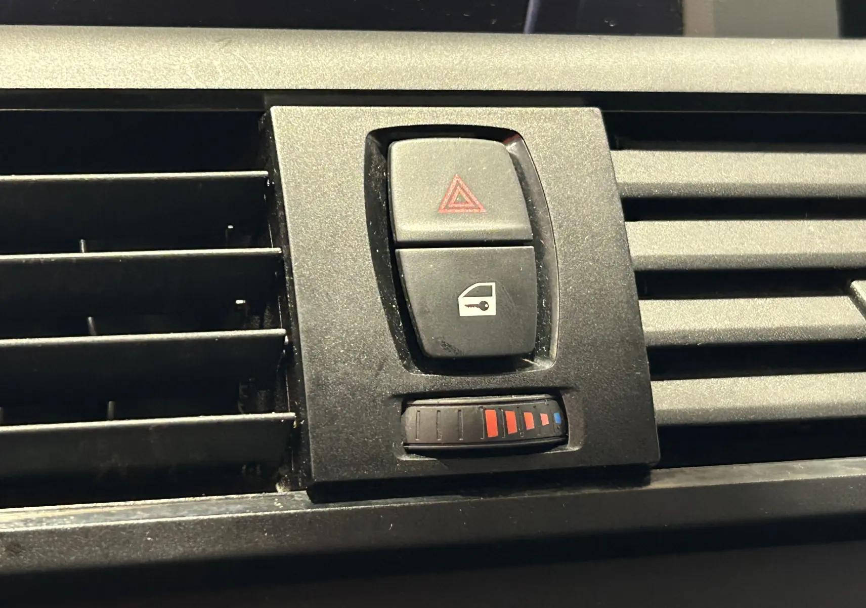Gros plan sur les commandes centrales de ventilation et alerte dans l'habitacle d'une BMW Série 1 gris diesel de 2014.