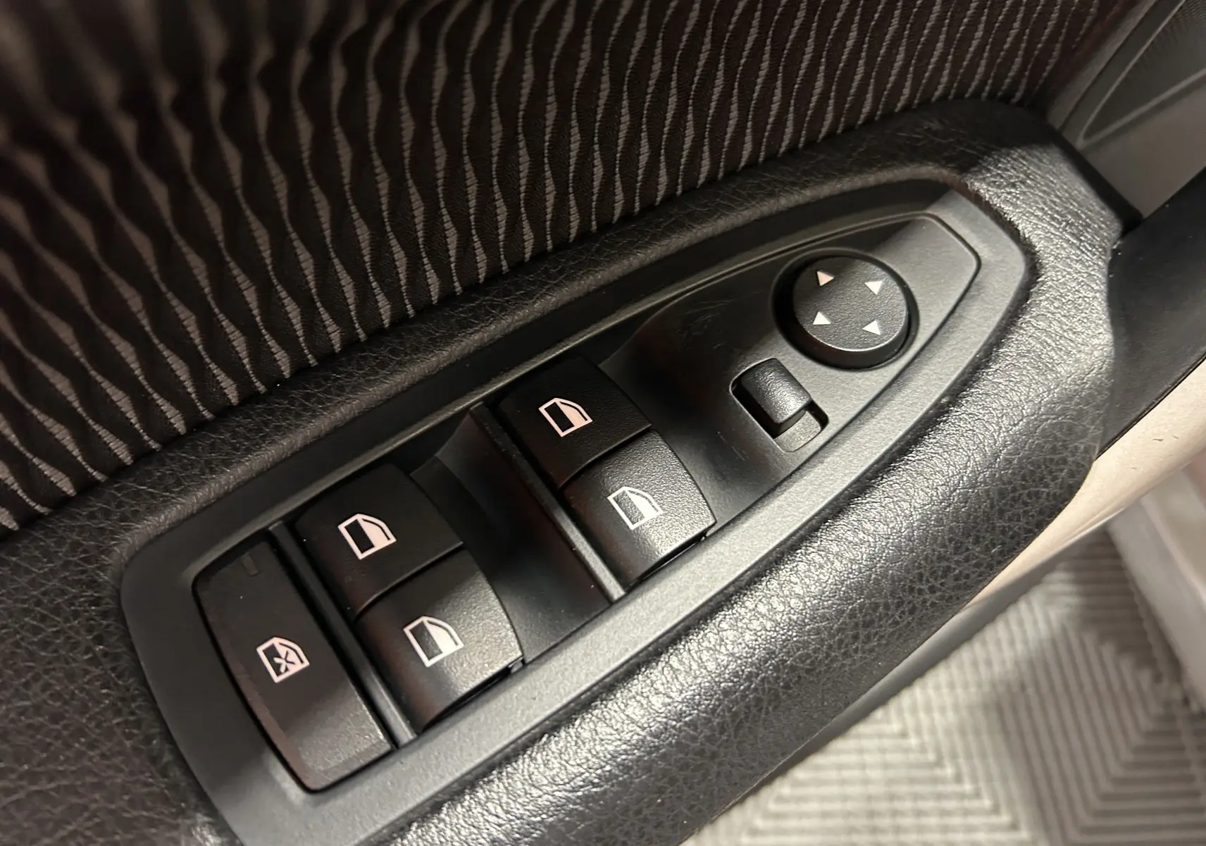Gros plan sur les commandes de lève-vitres et réglage des rétroviseurs côté conducteur d'une BMW Série 1 gris 2014.
