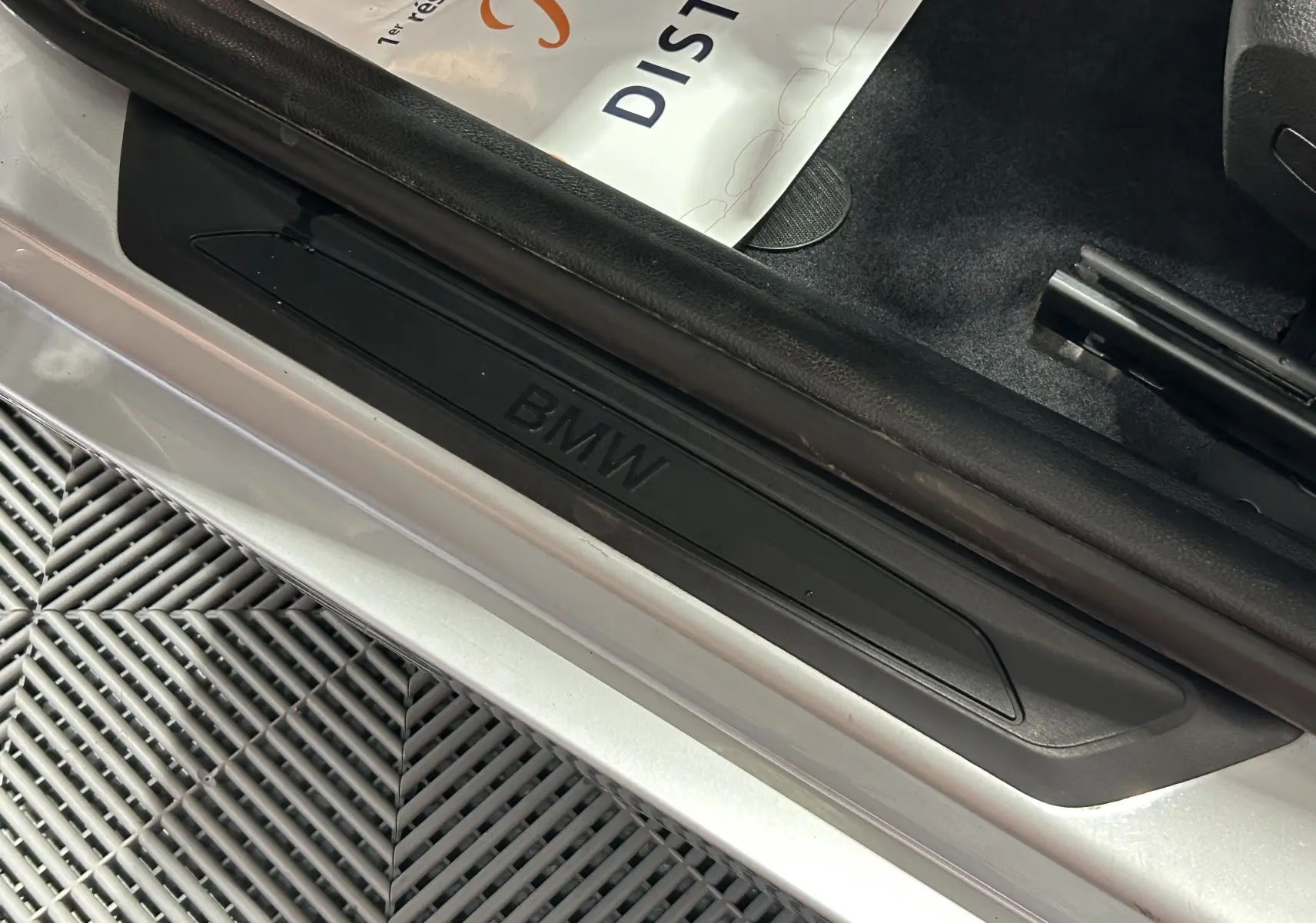 Gros plan sur la marche d'entrée noire avec logo BMW sur le côté gauche d'une BMW Série 1 gris 2014.