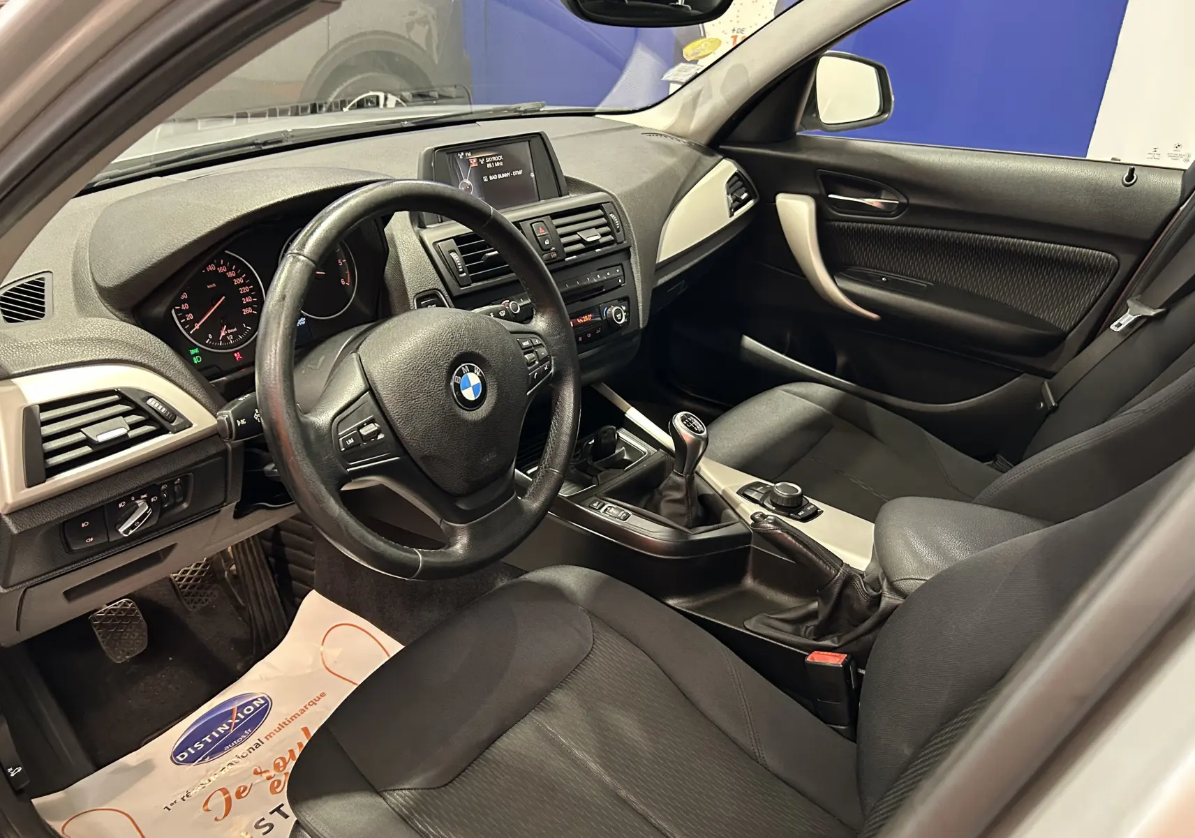 Intérieur de BMW Série 1 16d 2014 vu côté conducteur, tableau de bord noir avec volant cuir et boîte manuelle.