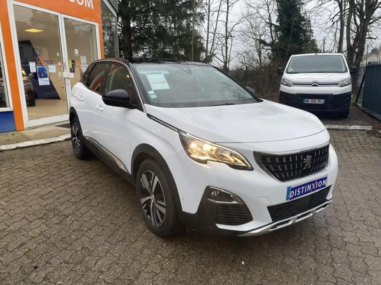 Peugeot 3008 blanc vue 3/4 avant droit avec toit noir et jantes alliage bi-ton sur parking extérieur.