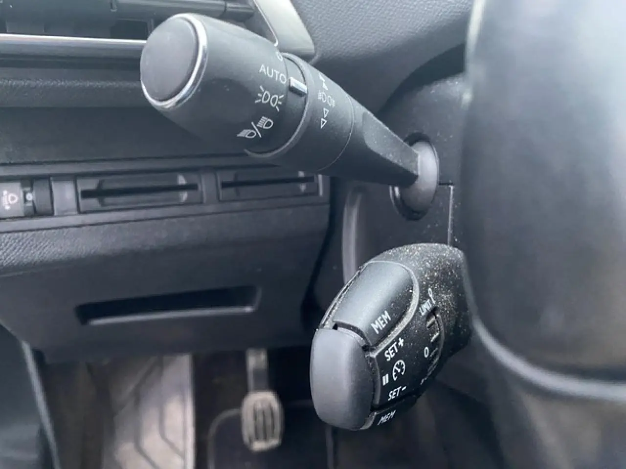 Gros plan sur la commande de régulateur de vitesse et commodo d'éclairage dans l'habitacle noir du Peugeot 3008 blanc 2017.