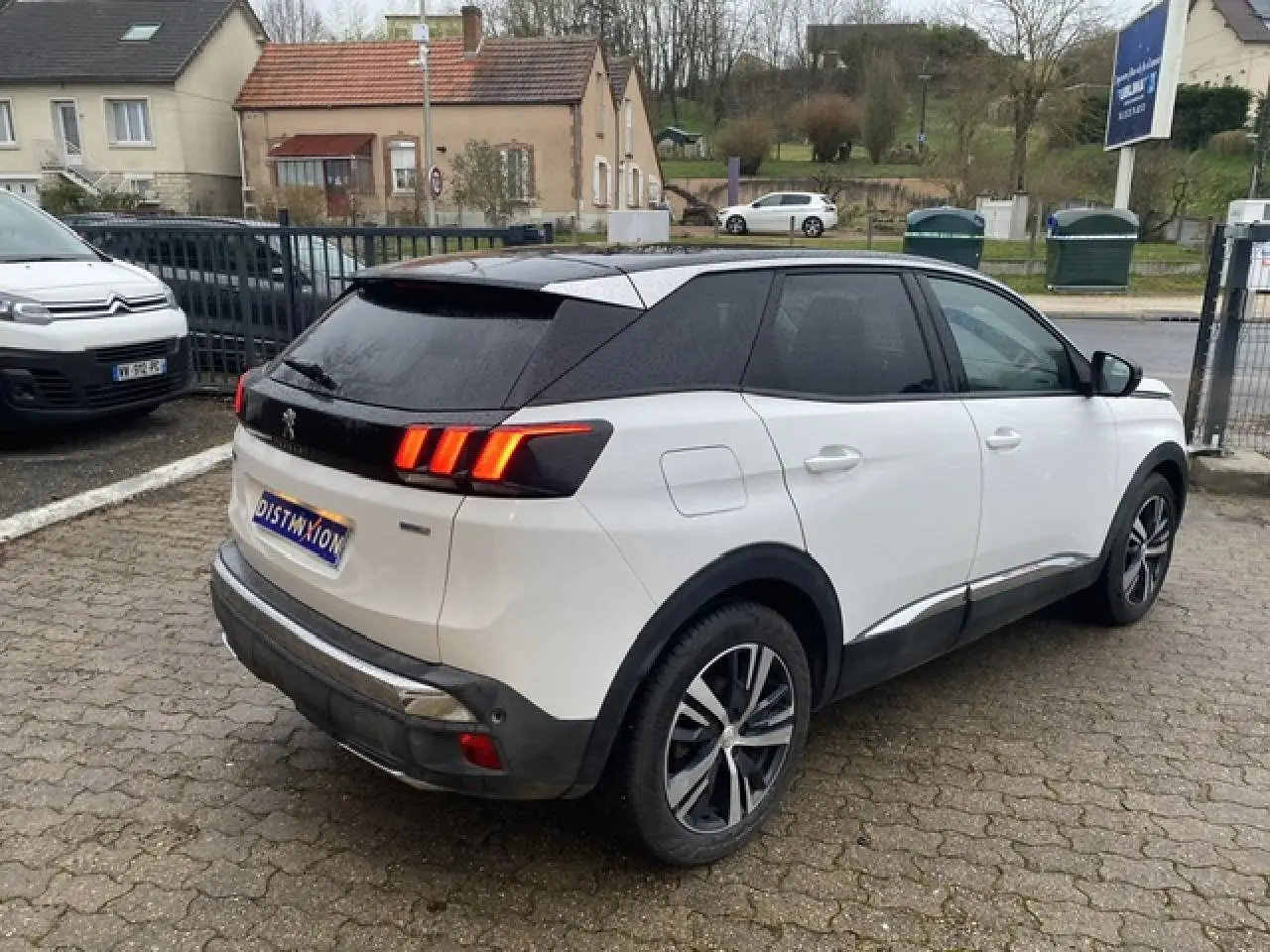 Peugeot 3008 blanc avec toit noir en vue 3/4 arrière côté droit, jantes alliage bi-ton et feux arrière allumés.