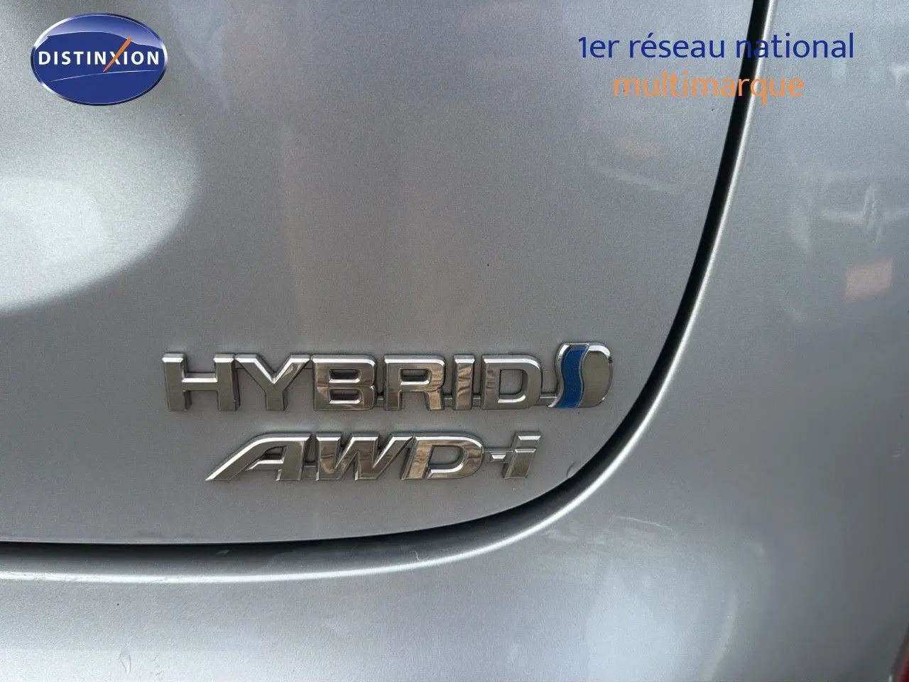 Gros plan sur l'emblème Hybrid AWD-i argenté sur la carrosserie gris minéral d'une Toyota Yaris Cross 2023.