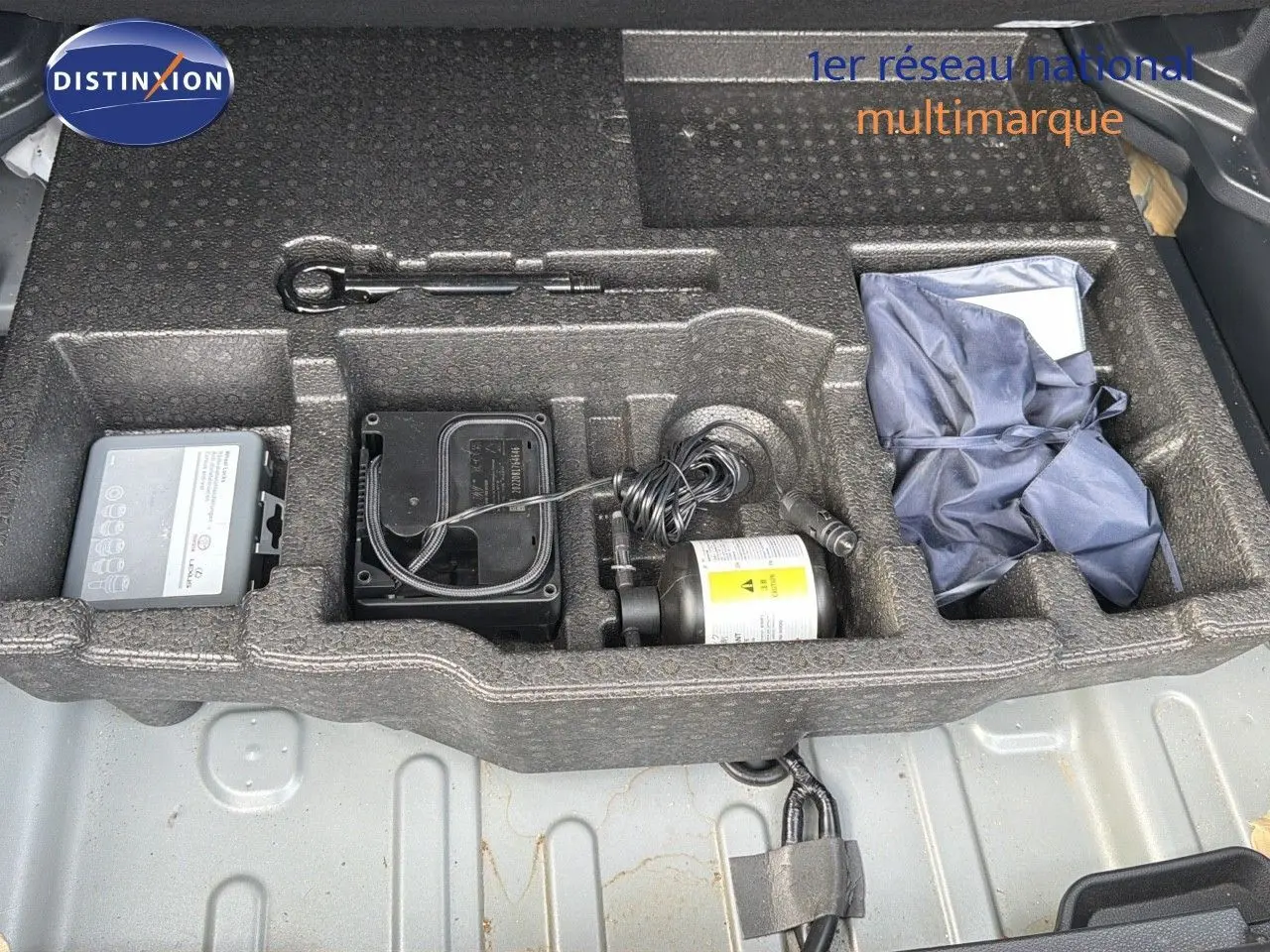 Compartiment de rangement sous le coffre de la Toyota Yaris Cross gris minéral, montrant outils et kit de réparation pneus.