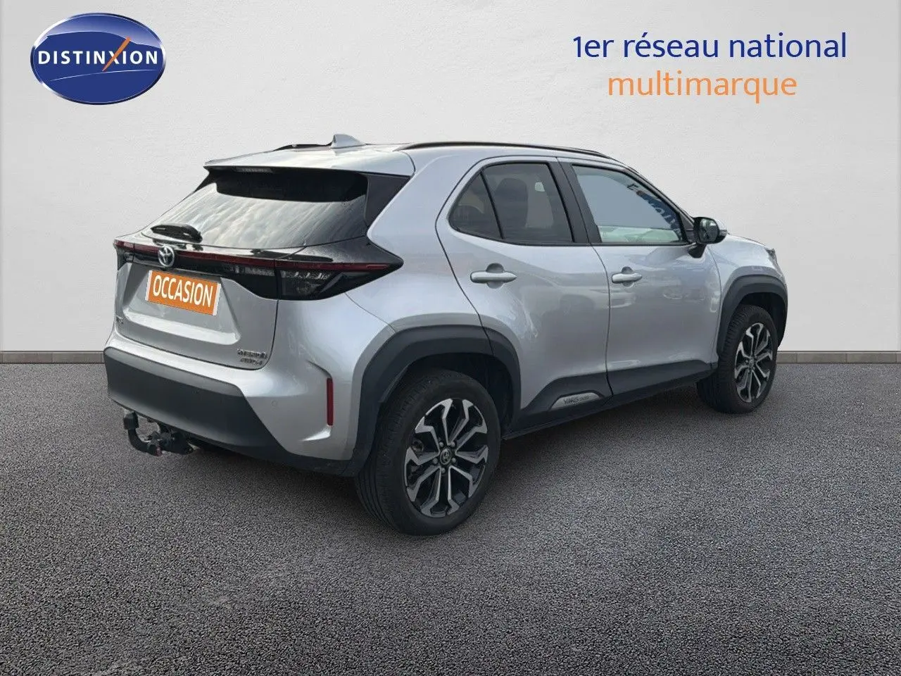 Toyota Yaris Cross gris minéral vue 3/4 arrière droit avec jantes bi-ton et attelage visible.