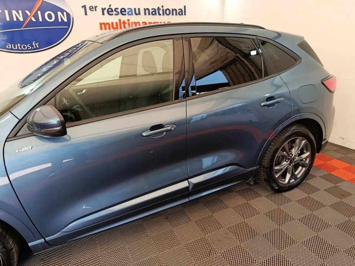 Vue latérale côté gauche d'un Ford Kuga bleu 2024 finition ST Line avec jantes alliage et rétroviseurs assortis.