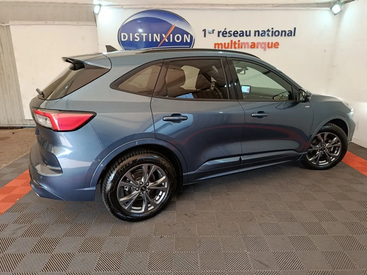Vue de profil côté droit d'un Ford Kuga 2024 bleu métallisé avec jantes alliage foncé dans un showroom.