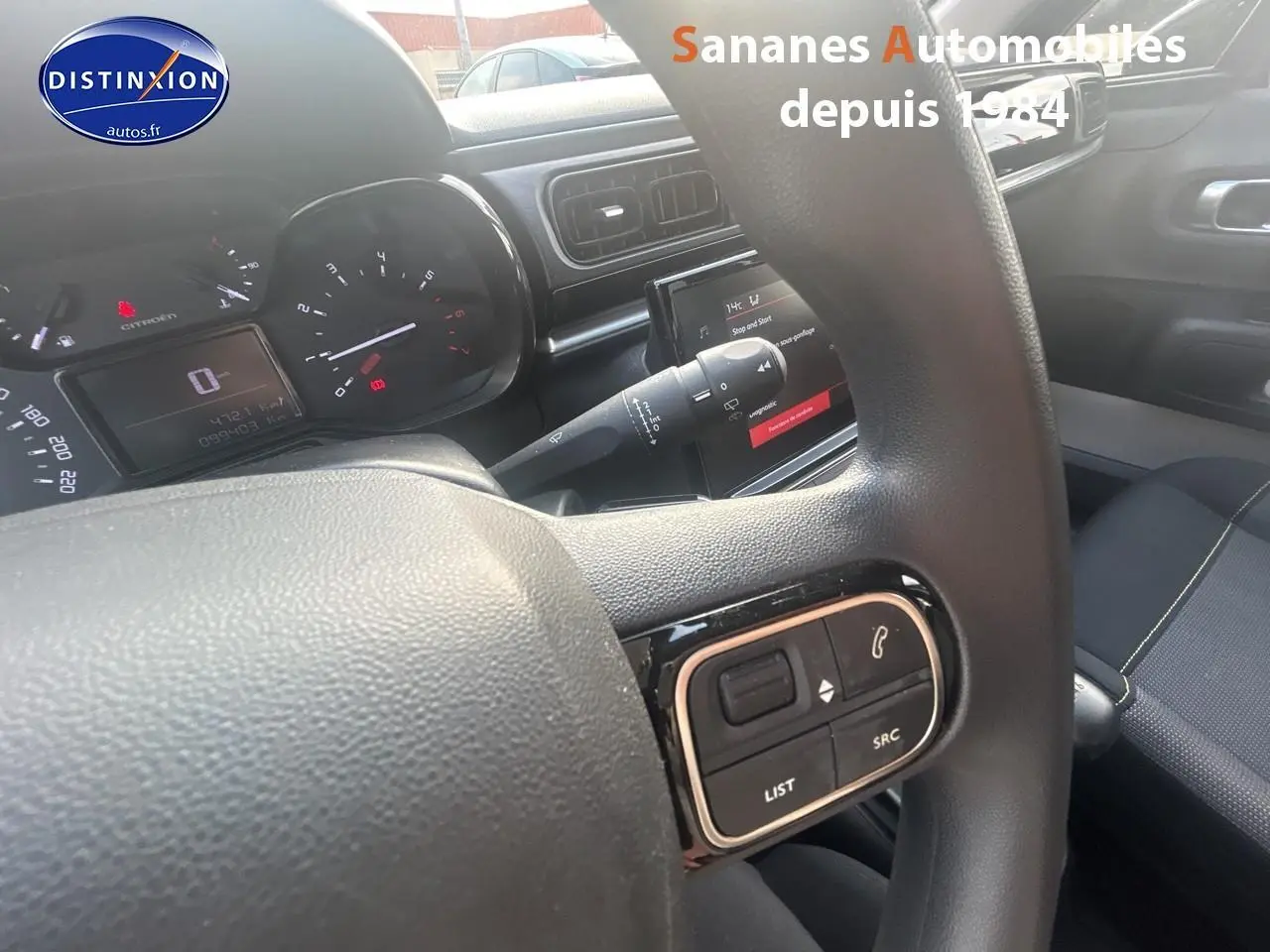 Vue intérieure centrée sur le volant et tableau de bord d'une Citroën C3 gris foncé avec commandes audio au volant.