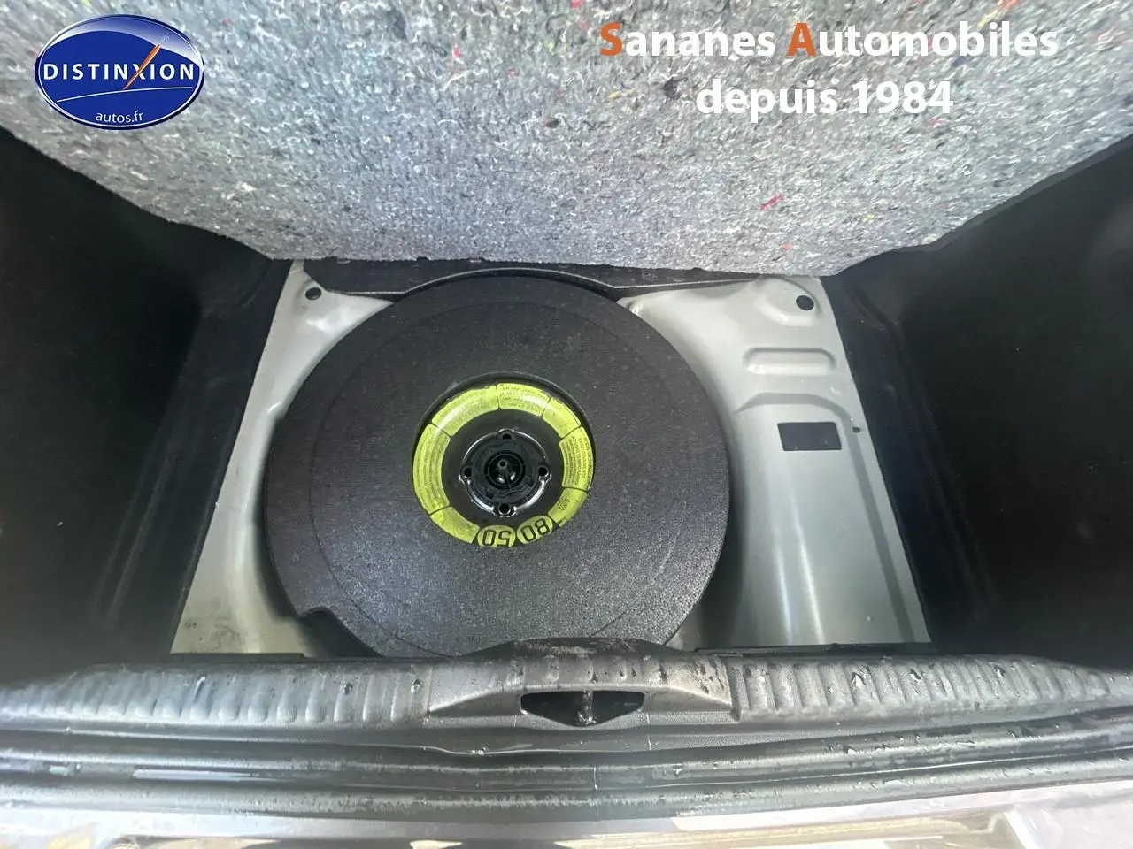 Vue plongeante sur la roue de secours galette dans le coffre d'une Citroën C3 gris foncé 2023.