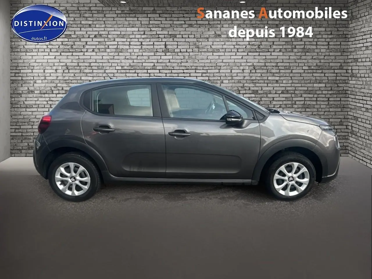 Profil côté droit d'une Citroën C3 gris foncé 2023, avec jantes alliage et rétroviseurs noirs, sur fond brique.