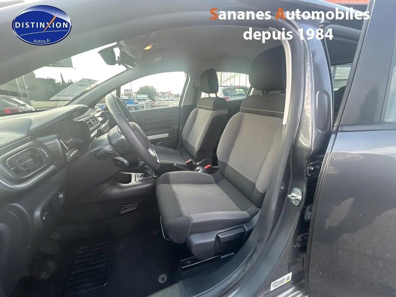 Vue intérieure côté conducteur d'une Citroën C3 gris foncé 2023, mettant en valeur les sièges tissu Mica Grey et la boîte manuelle.