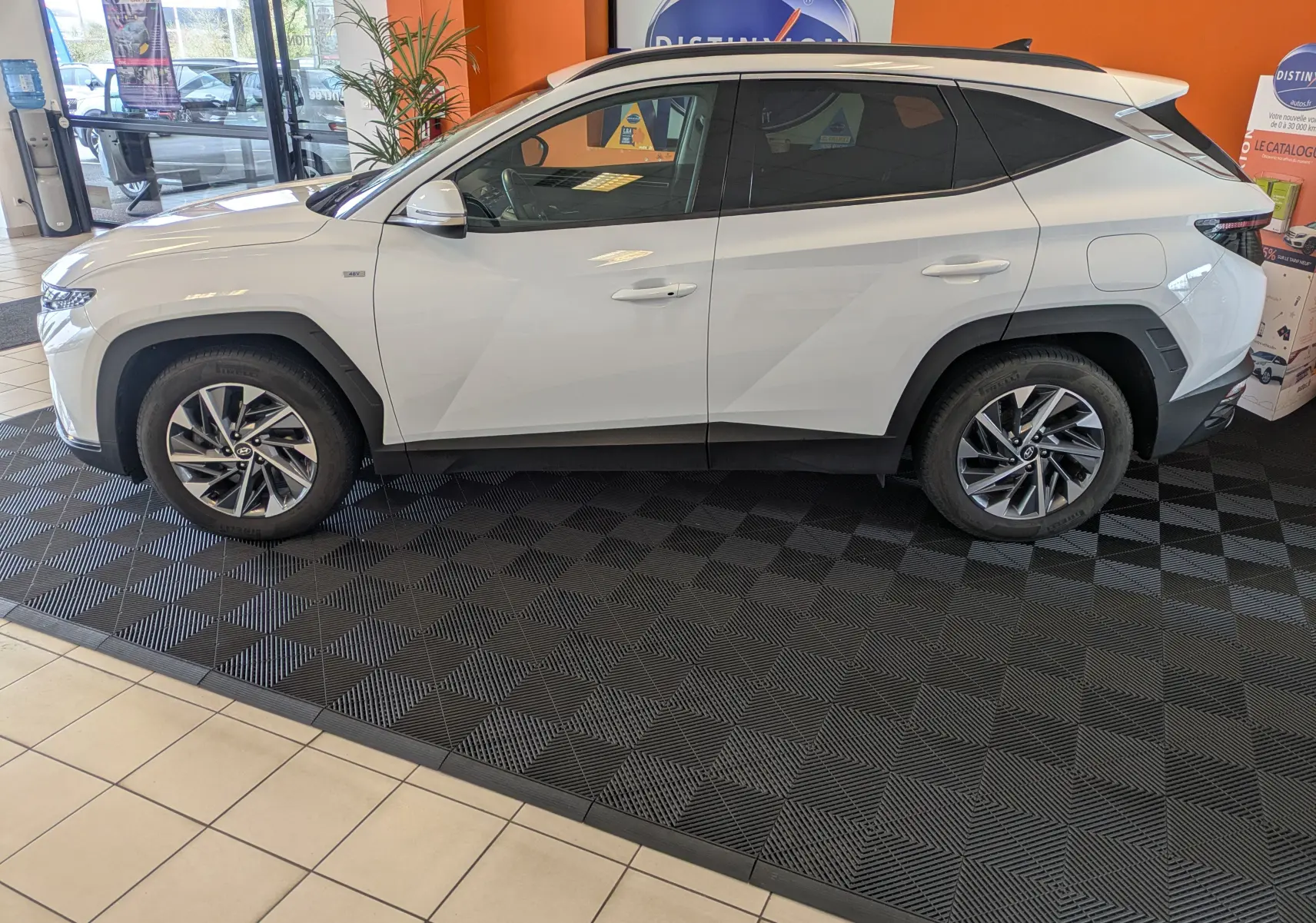 Vue de profil côté gauche d'un Hyundai Tucson blanc 2021 avec jantes alliage et vitres teintées en showroom.