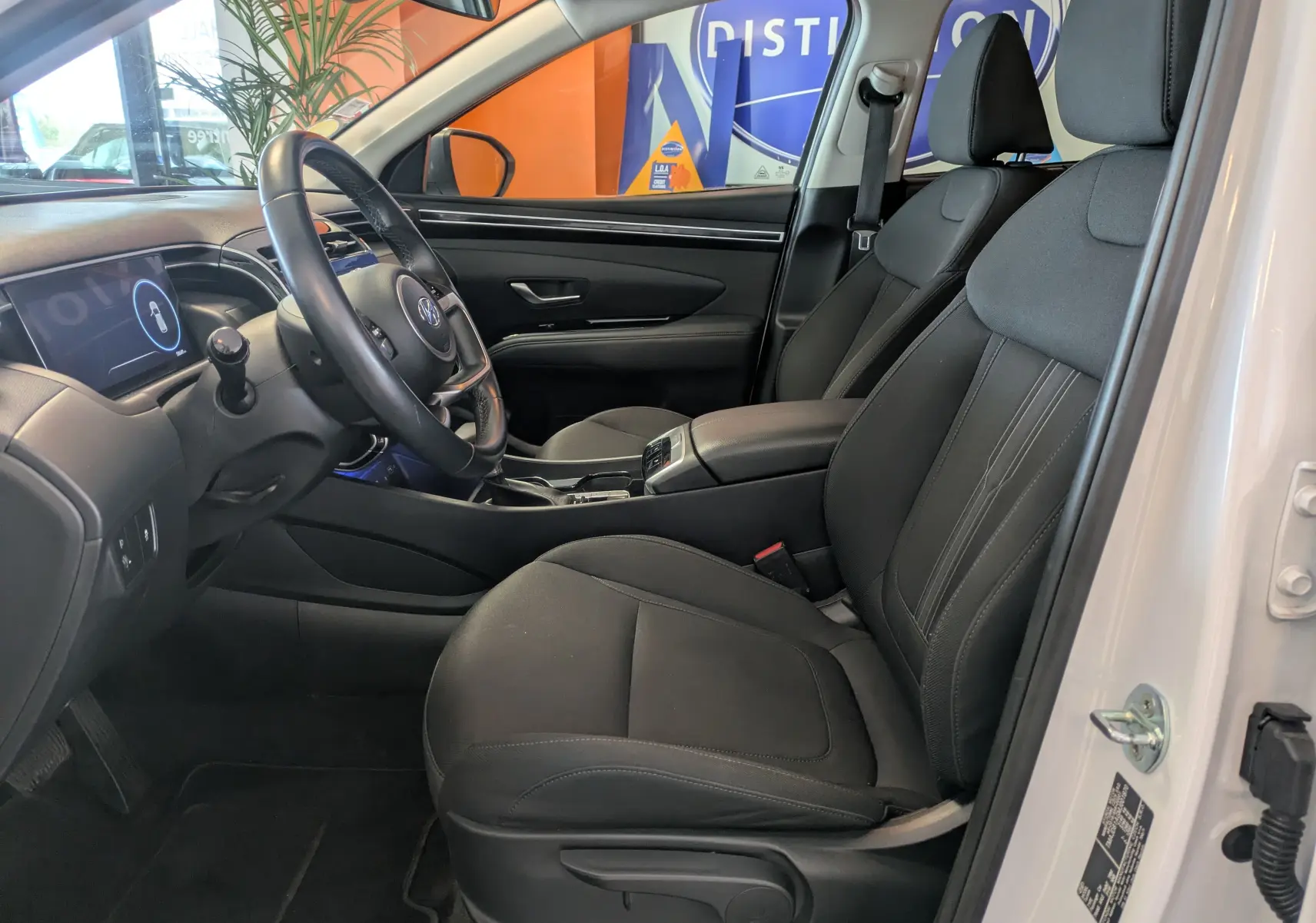 Vue intérieure côté conducteur du Hyundai Tucson blanc 2021, sièges noirs, volant multifonction et tableau de bord digital.