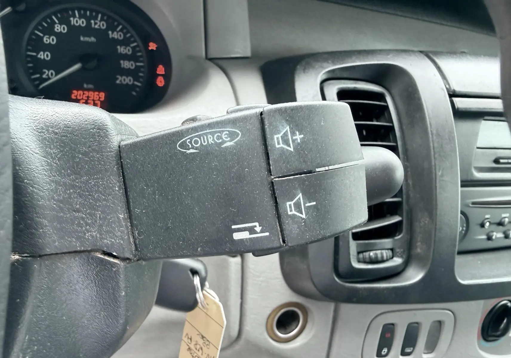 Gros plan sur la commande audio au volant du Nissan Primastar blanc, avec tableau de bord et compteur en arrière-plan.