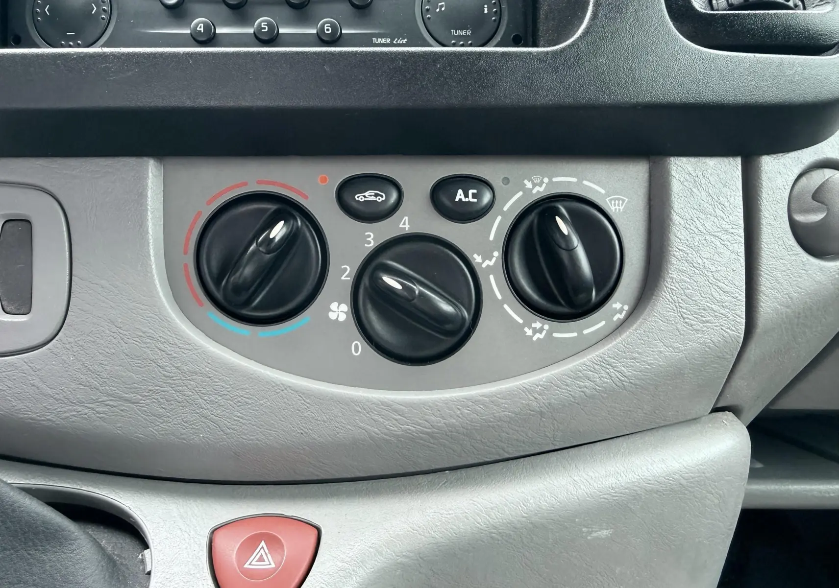 Gros plan sur les commandes de climatisation grises du tableau de bord du Nissan Primastar blanc de 2005.