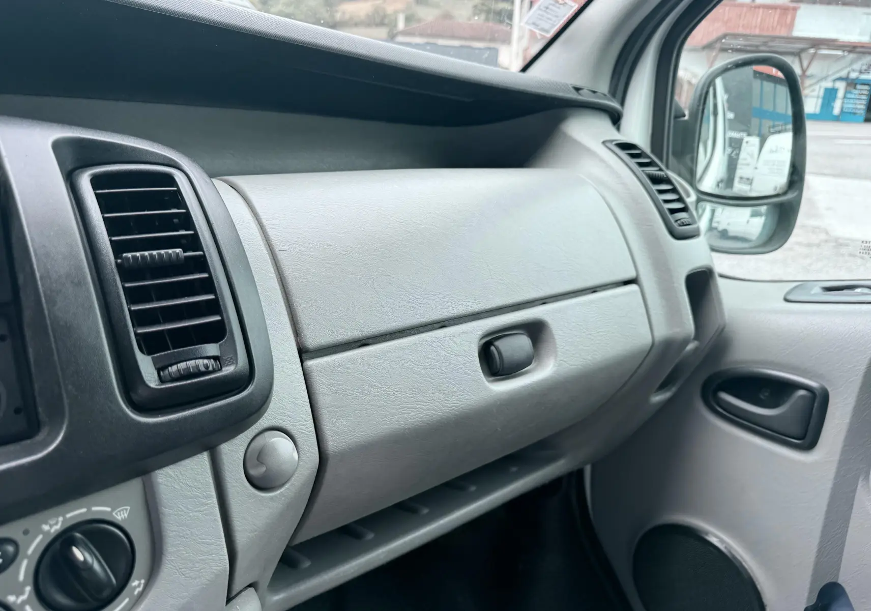 Intérieur gris clair du tableau de bord côté passager du Nissan Primastar blanc, avec porte-gants fermé et aérateurs visibles.