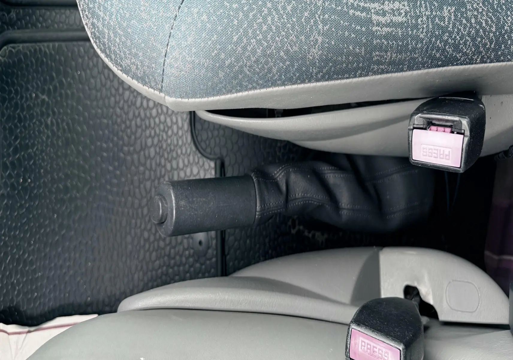 Détail intérieur montrant les ceintures de sécurité et frein à main entre les sièges tissu gris-bleu du Nissan Primastar.