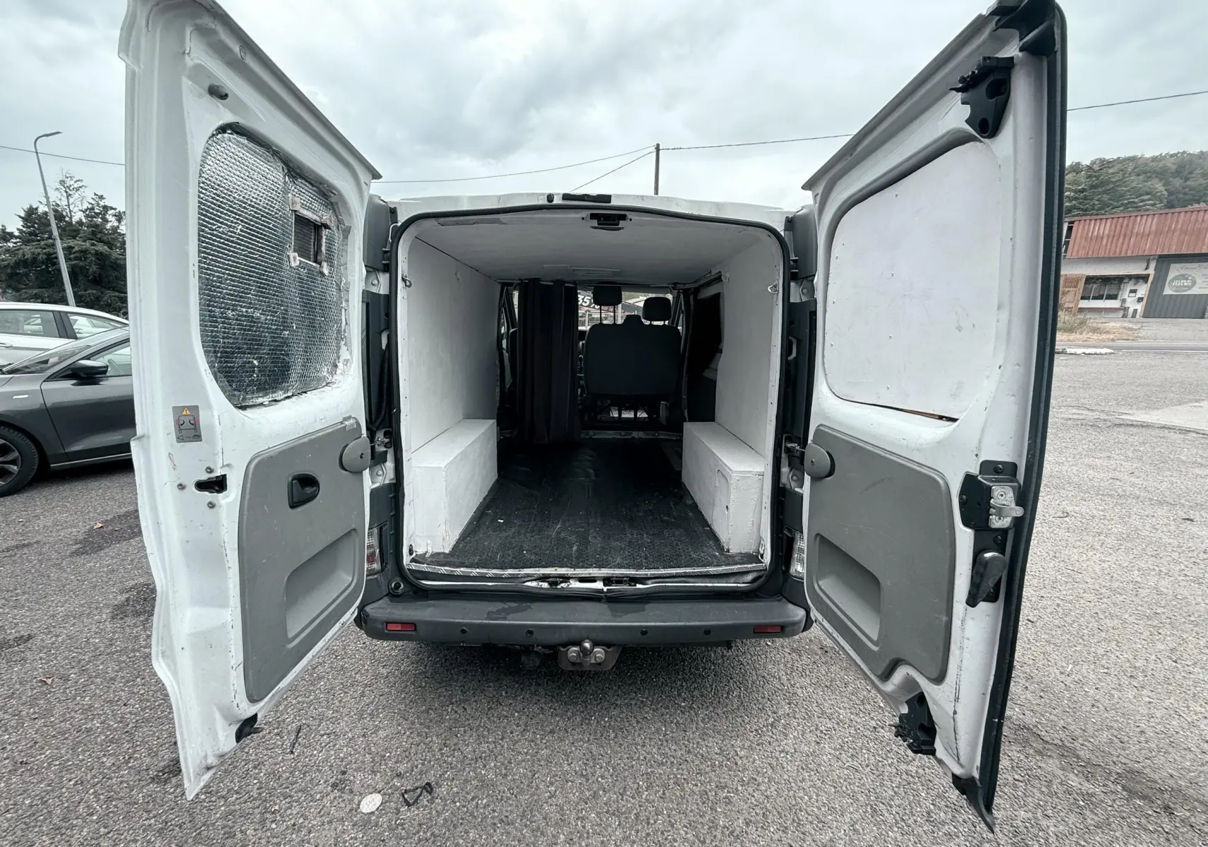Vue arrière ouverte du Nissan Primastar blanc de 2005 montrant l'espace de chargement vide et les portes battantes ouvertes.