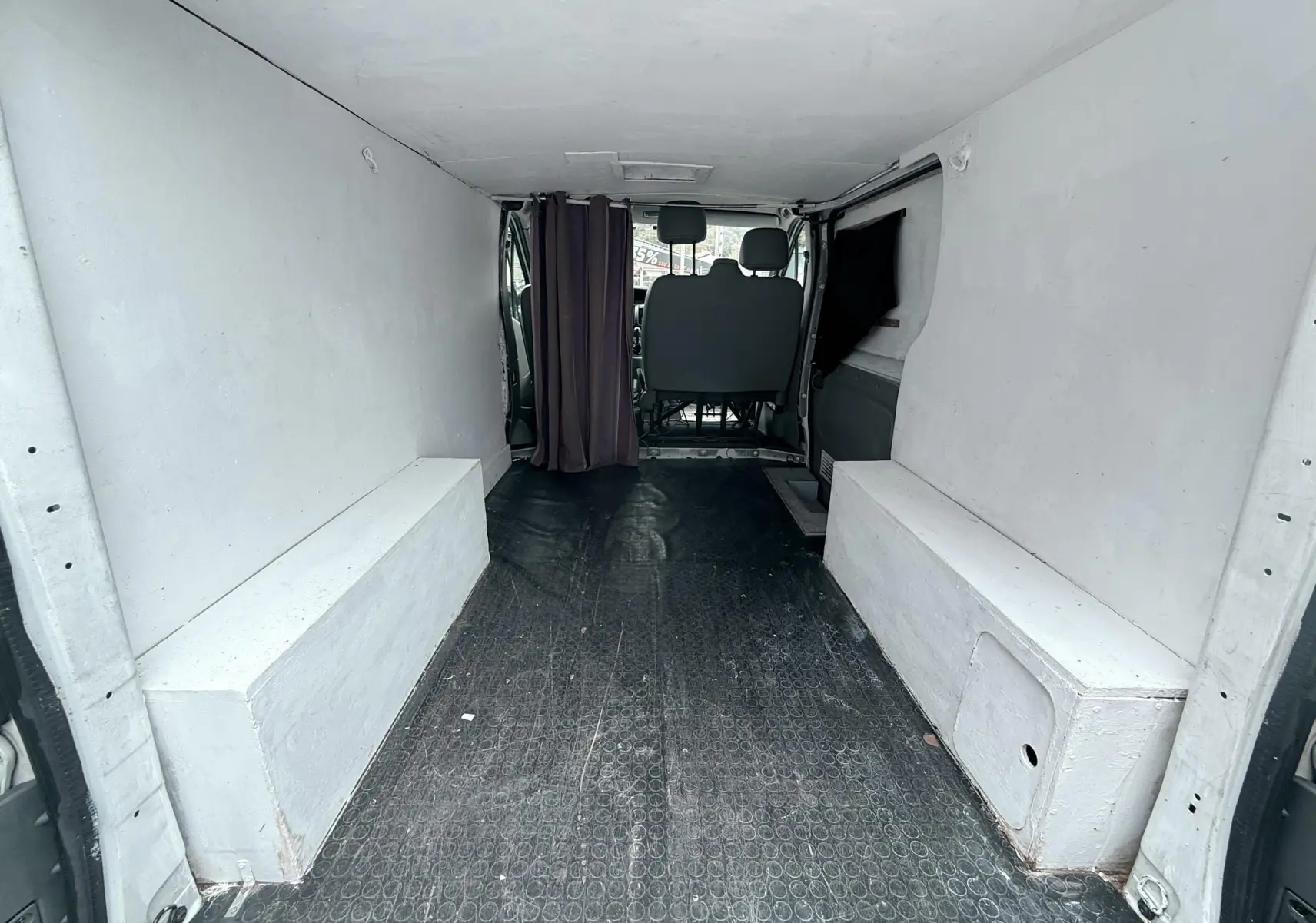 Vue intérieure arrière du Nissan Primastar blanc de 2005, montrant l’espace de chargement vide avec banquettes latérales blanches.